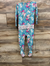 Back view of RuffleButts SoftSnooze footie showing seat ruffles, teal floral print and pink grippy soles on wood backdrop