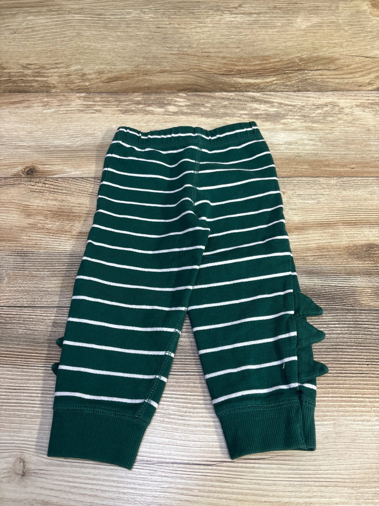 Flat lay of Carter’s green striped pull-on joggers 18M showing elastic waist, cuffed ankles, and side spikes on wood floor