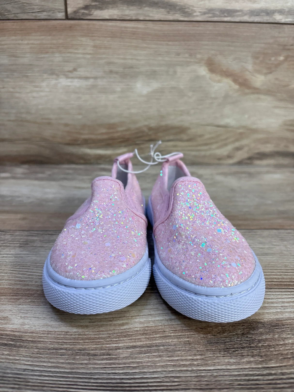 Front view of Cat & Jack Yana toddler slip-on sneakers with pink glitter upper and white rubber sole on wood background
