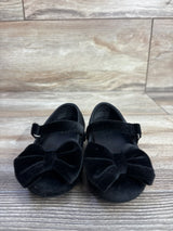 Front view of Baby Gap velvet Mary Jane flats in black showing bow accent and hook-and-loop strap on wood floor background