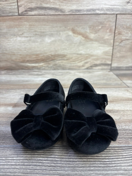 Front view of Baby Gap velvet Mary Jane flats in black showing bow accent and hook-and-loop strap on wood floor background