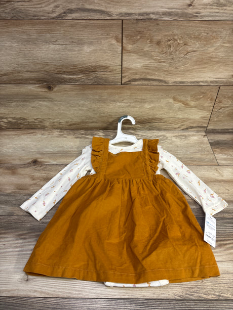 Front view of a mustard corduroy skirtall over a white patterned long-sleeve bodysuit on a hanger with a wood background