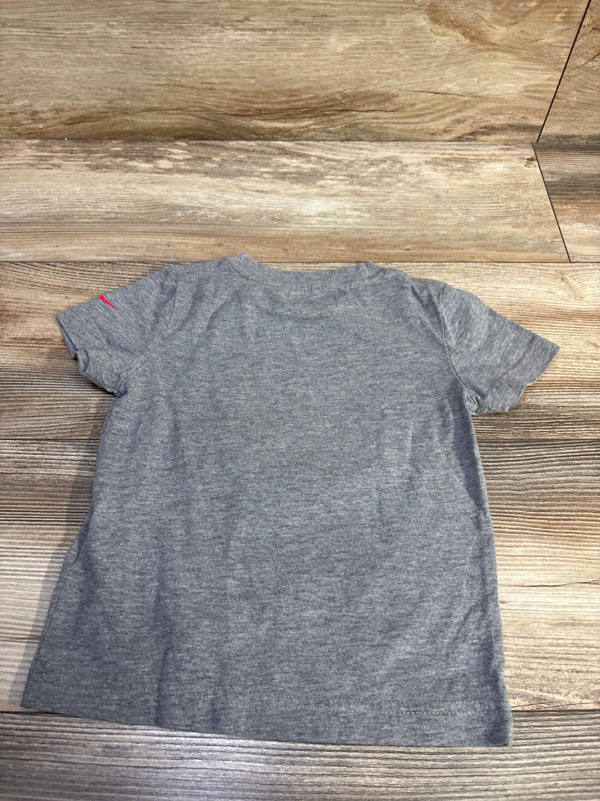 Front view of a gray Nike toddler shirt in size 3T, showcasing short sleeves and a red swoosh logo on a wood-grain background