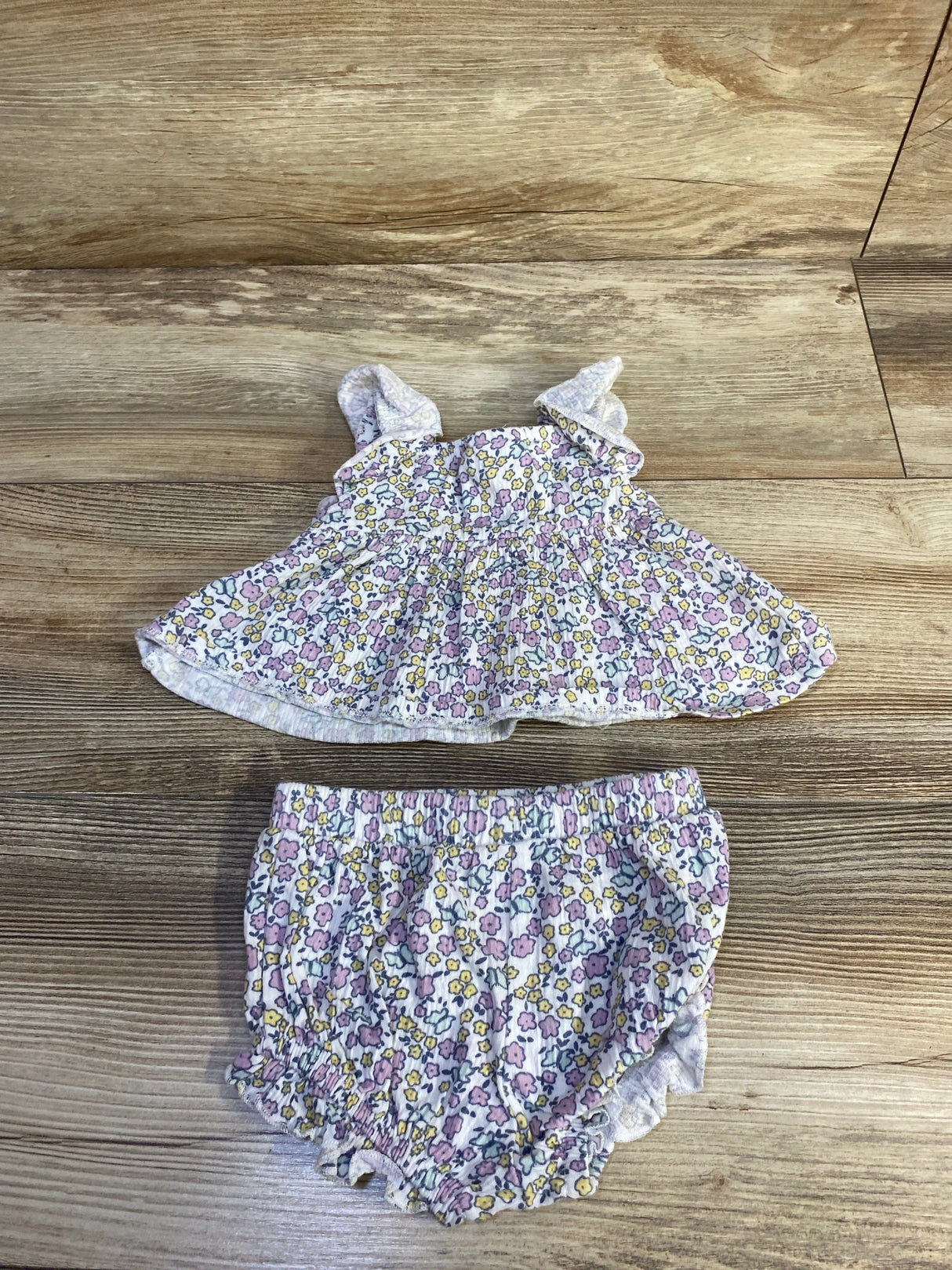 Flat lay of Nicole Miller smocked floral shirt and matching bloomers with ruffled straps and elasticized legs on wood floor