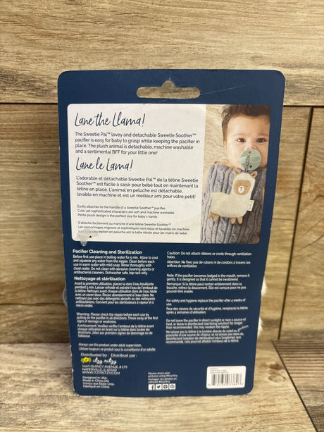 Back of Itzy Ritzy Sweetie Pal Pacifier Lane the Llama package showing detachable llama plush and pacifier on wood