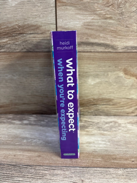 Spine view of What to Expect When You’re Expecting 5th Edition paperback book with purple cover on wood background