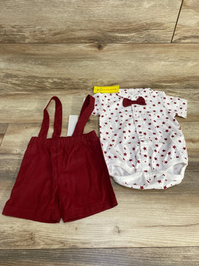 Top-down view of baby 2-piece set: white star-print bodysuit with red bow and red suspender shorts on wood floor