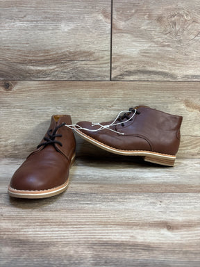 Brown leather kids chukka boots with black laces on wood floor background