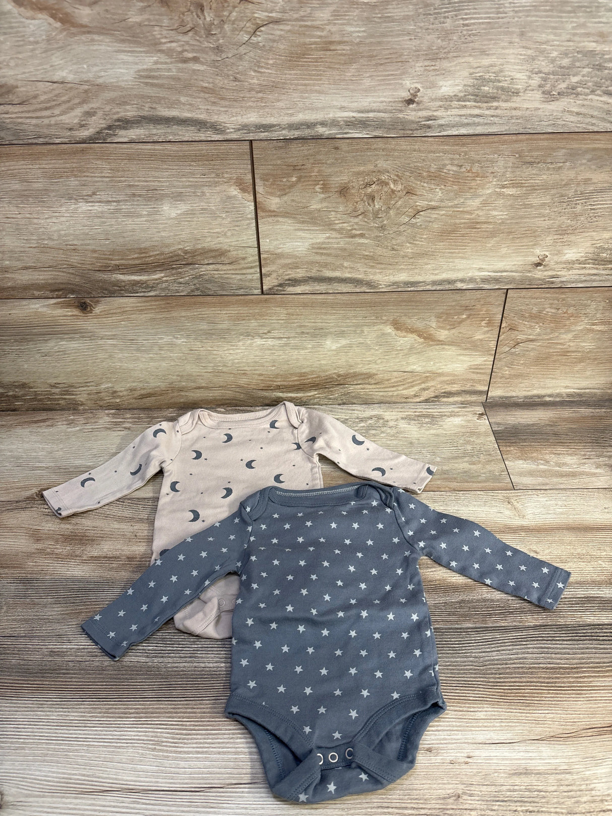 Flat lay of two Cloud Island long-sleeve bodysuits (3-6 months) showcasing moon and star prints on a wood background