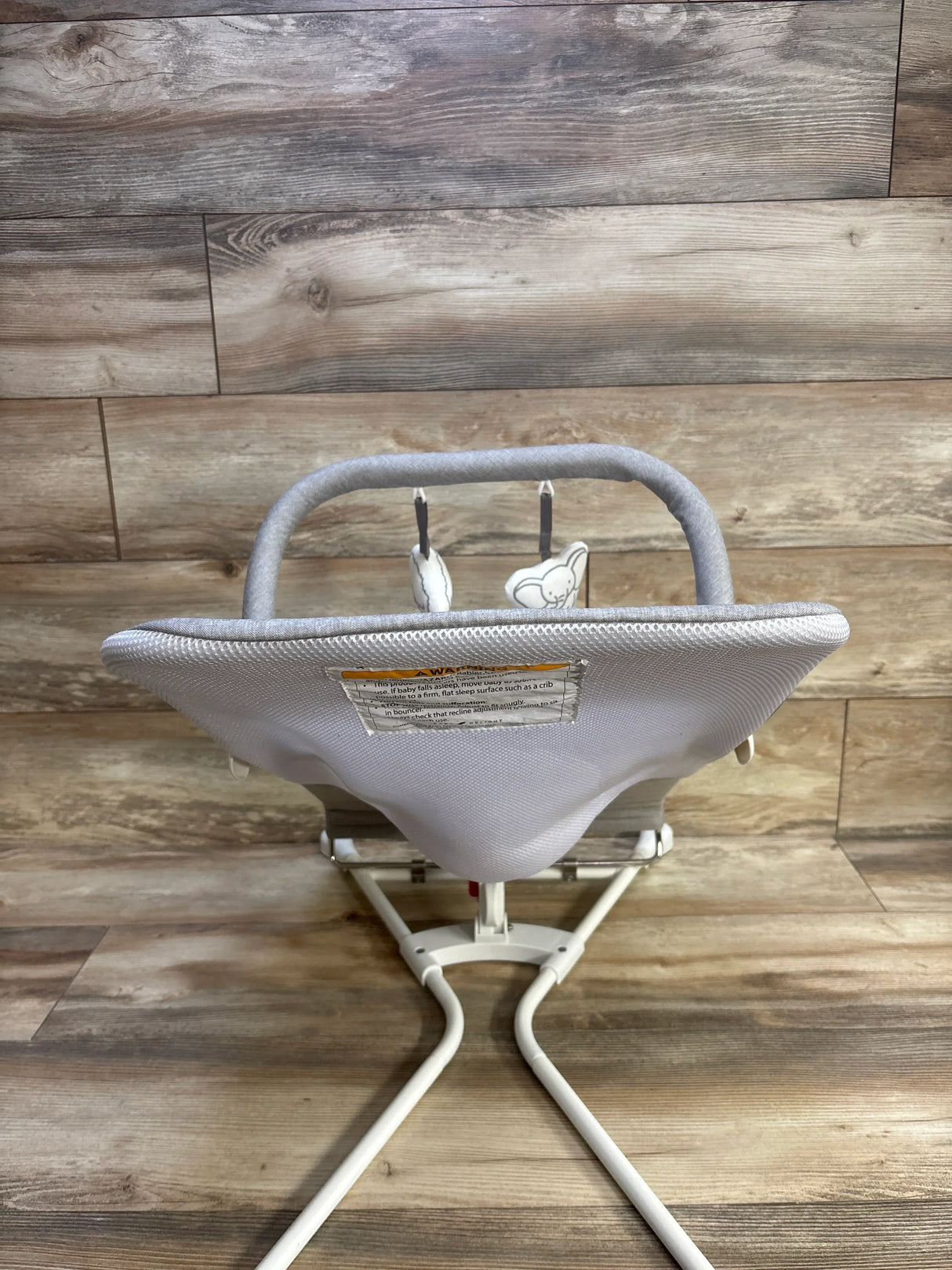 Rear view of Baby Delight Highland bouncer in pebble grey with mesh seat, two hanging toys, and white metal frame