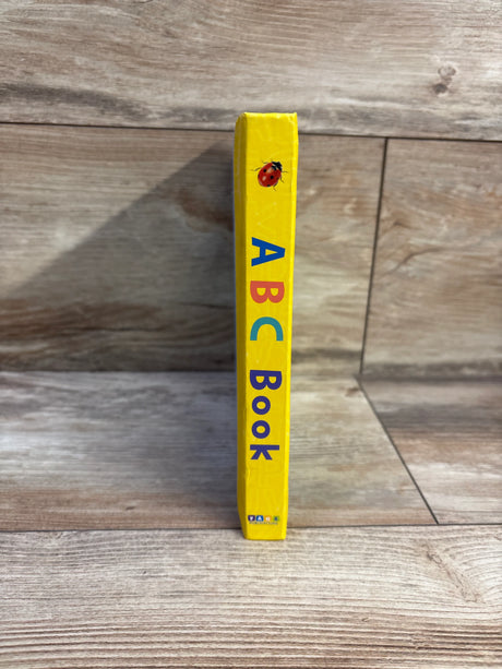 Spine view of ABC board book showcasing yellow spine with multicolored letters A B C and ladybug illustration on a wooden floor background