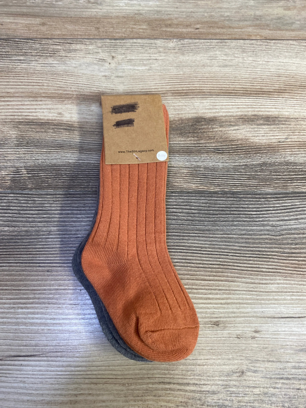 Top-down view of ribbed baby socks 2-pack in rust orange and charcoal, size 0-12 months on wood background