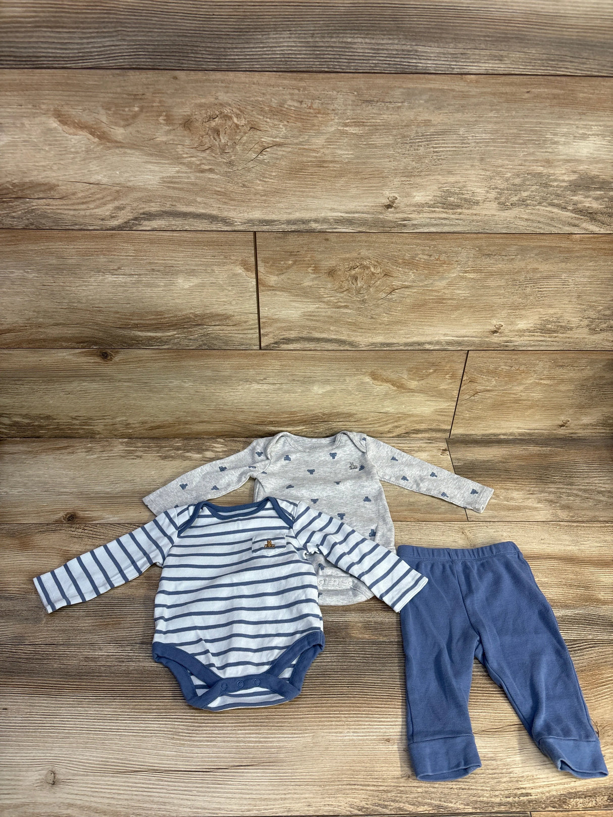 Flat lay of Baby Gap 3-piece set: navy-striped bodysuit, grey bear-print bodysuit, and navy pants on wood backdrop