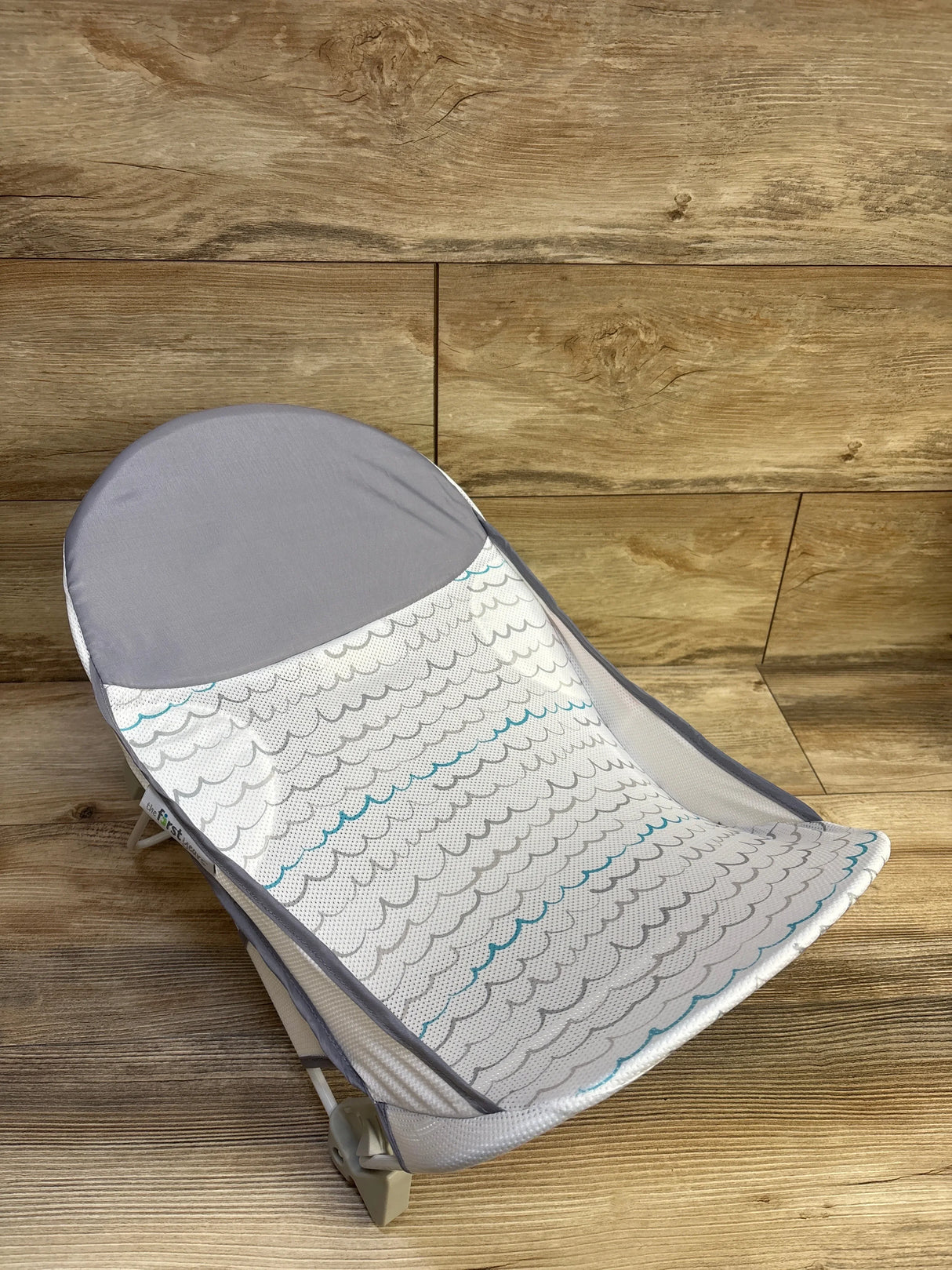 Angled top view of Summer Deluxe baby bather in grey with mesh wave-patterned sling and padded headrest on wood-look floor
