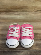Front view of pink Converse Cribster baby shoes showing white rubber toe caps and laces on wood tabletop