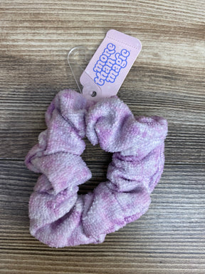 Purple and white textured fabric scrunchie with 'more than magic' tag on wood surface