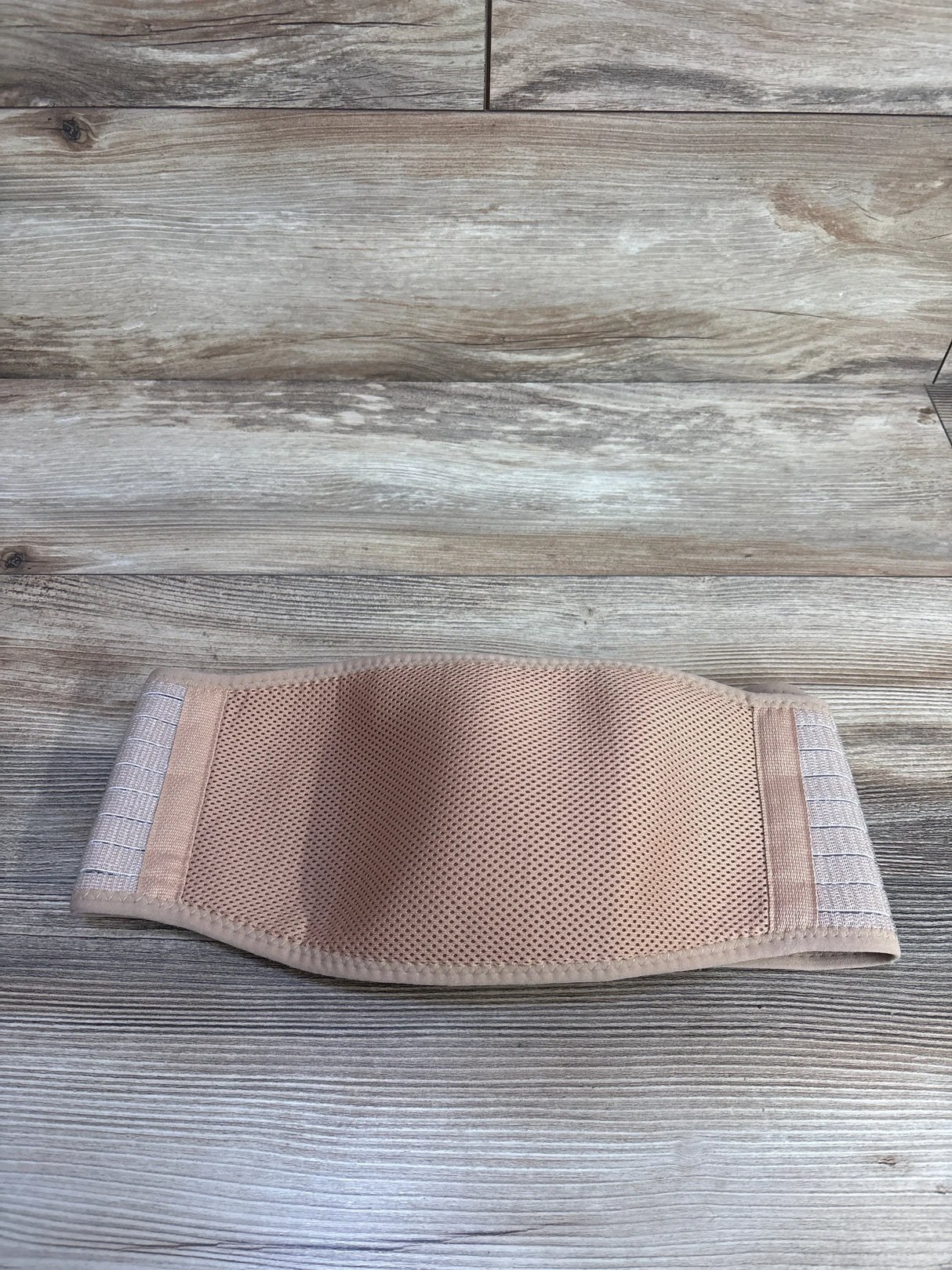 Flat lay of AJ Maternity beige belly band showcasing breathable mesh fabric and Velcro straps on wood background