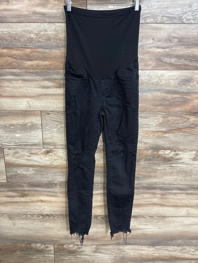 Front view of black SONG maternity full-panel distressed jeans showing high elastic belly panel, ripped knees and frayed ankle hems on wood background