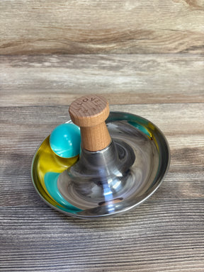 Angled view of Lovevery Stainless Steel Tip and Turn: stainless bowl, wooden LOVE knob, teal-yellow ball on wood background