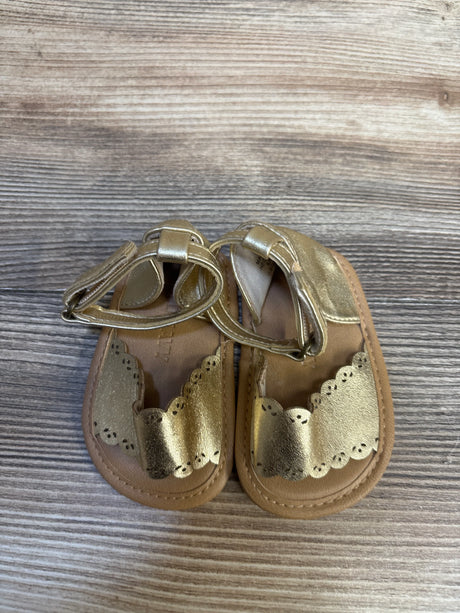 Gold baby sandals with scalloped edges on wood background