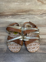 Brown and gold toddler sandals with MK logo print on wood background