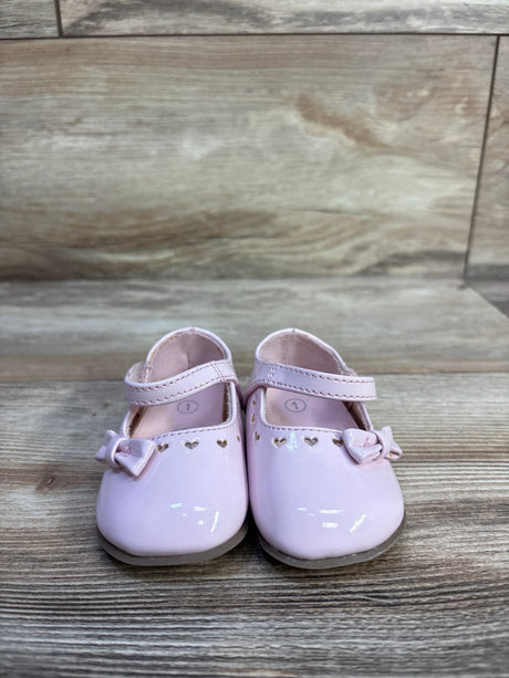 Front view of Teeny Toes patent Mary Jane baby flats in pink showing heart cutouts and bows on a wood plank background