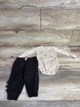 Flat lay of beige long-sleeve dinosaur bodysuit and black pants showing dinosaur prints and ruffle spikes on light wood