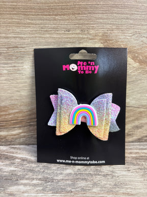 Front view of glitter pastel rainbow hair bow with rainbow applique center on black display card over wood background