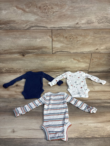 Three baby onesies: solid navy, striped gray, and white with animal print, laid on wood floor for resale.
