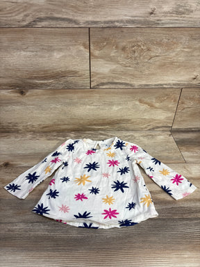 White long-sleeve toddler shirt with pink, navy, and yellow flower patterns on wooden floor