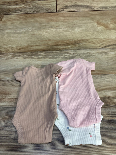 Top-down view of three preemie ribbed short-sleeve bodysuits (dusty pink, light mauve, and white floral) on wood background