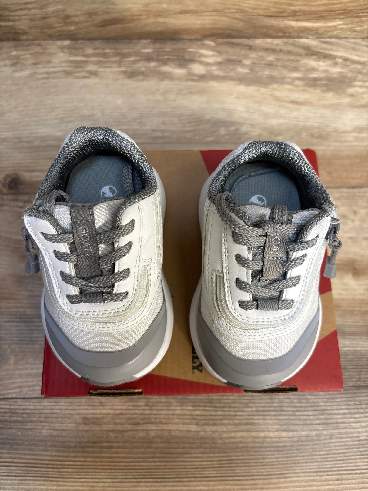Gray and white toddler sneakers with laces on a shoe box, wooden floor background