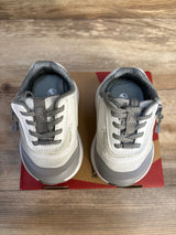 Gray and white toddler sneakers with laces on a shoe box, wooden floor background