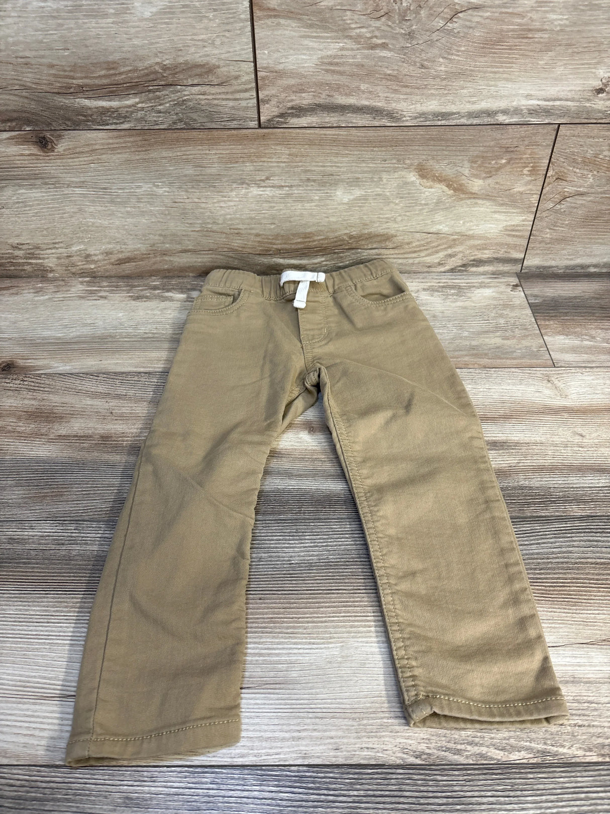 Kids khaki pants with white drawstring, laid on wooden floor