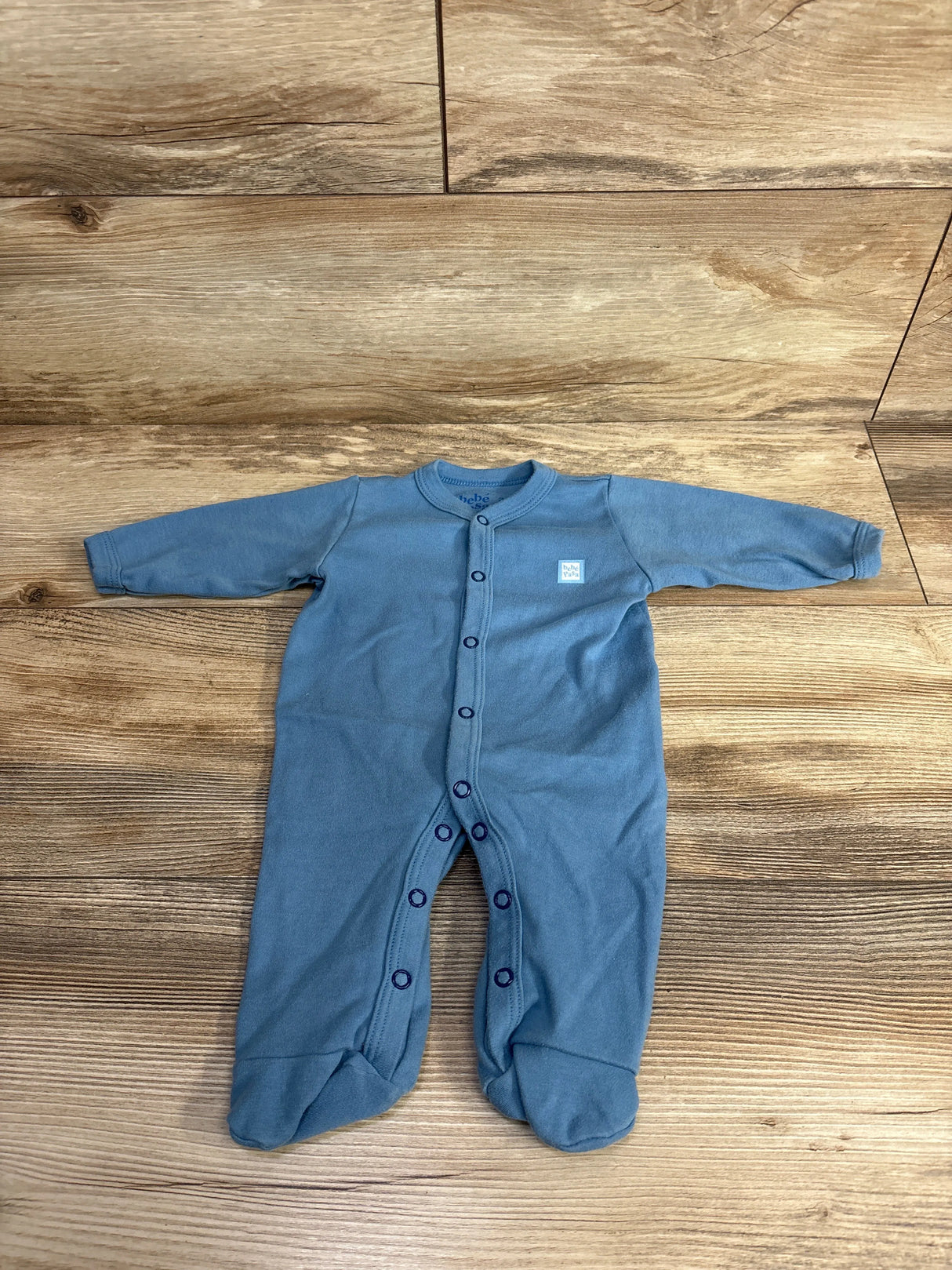 Blue long-sleeve baby onesie with snap buttons and feet, laid out on wooden floor