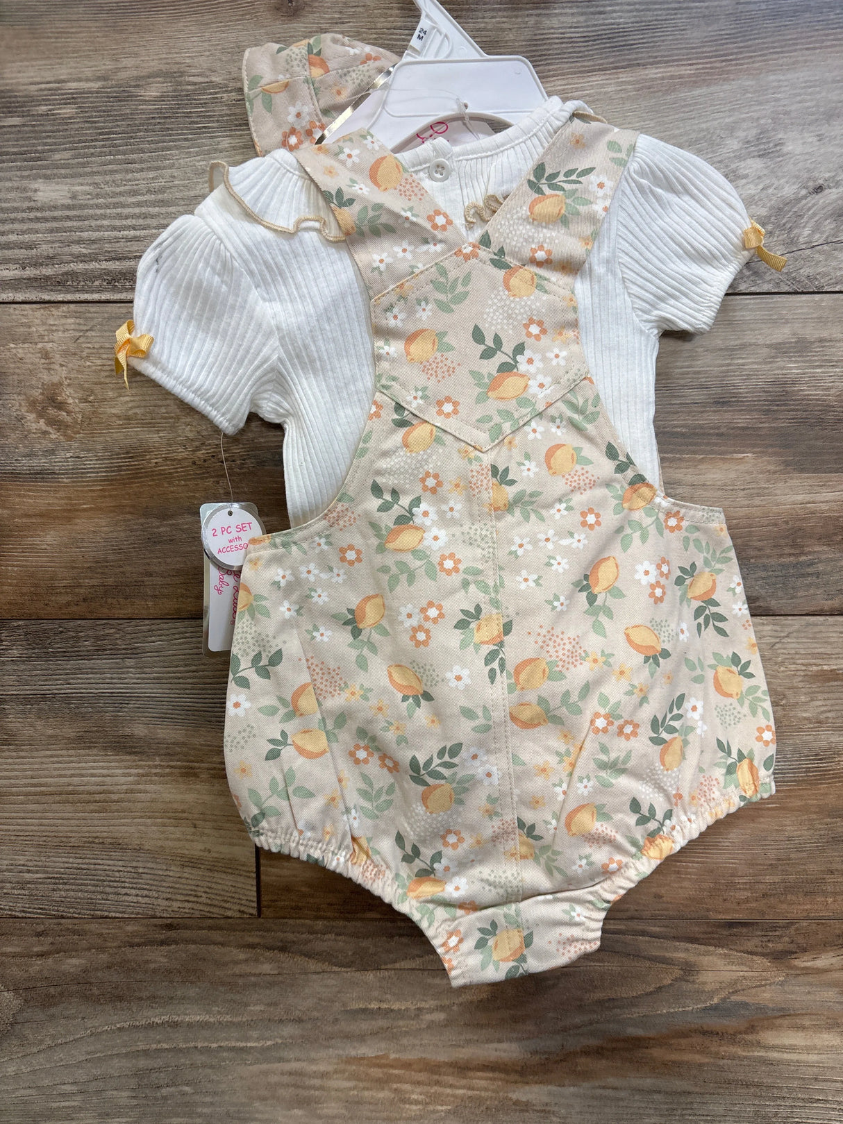Front view of 2-piece baby shirt and lemon-print shortalls set with white ribbed top and bow accents on wooden background