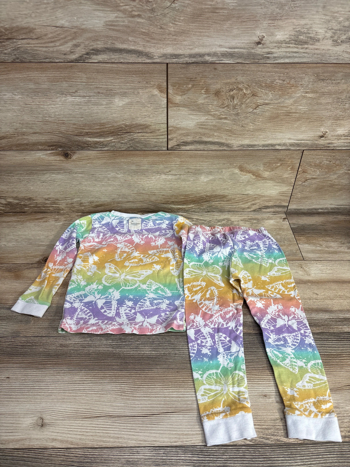 Children's two-piece pajama set with multicolor rainbow background and white butterfly print on wooden floor