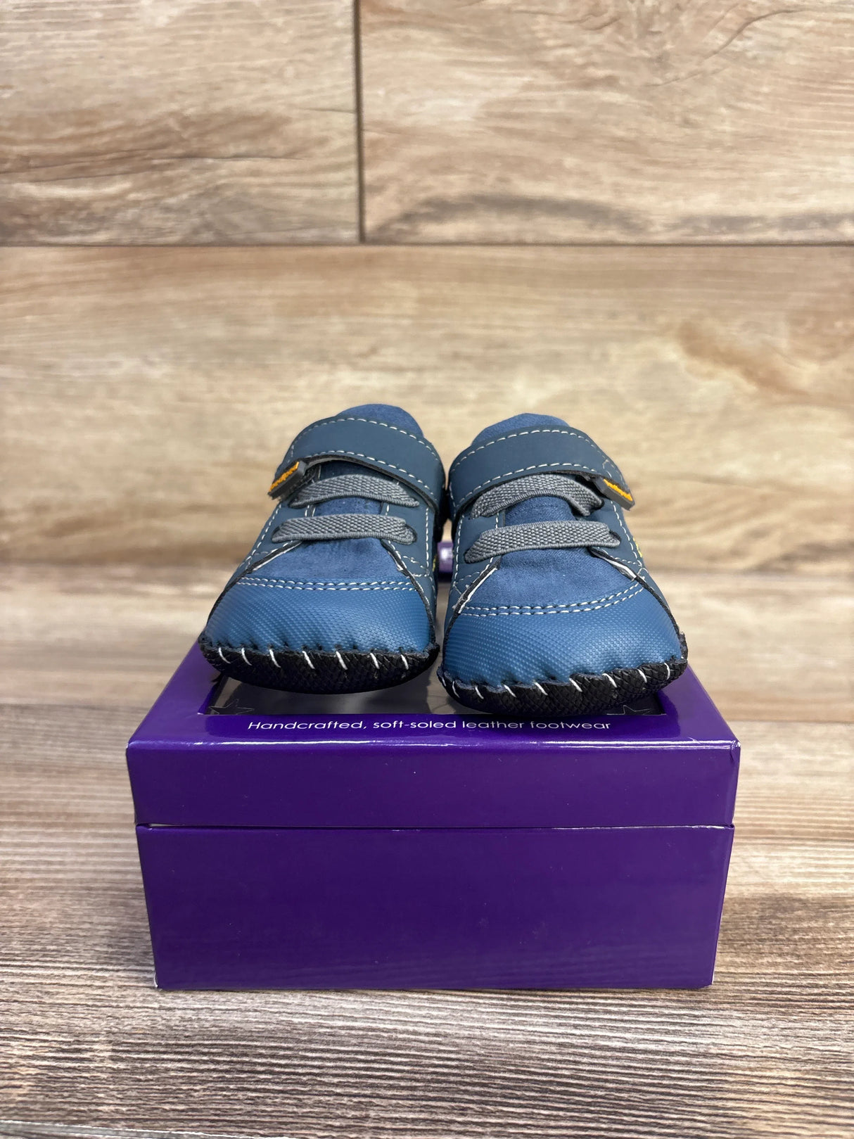 Front view of Pediped Dani navy crib shoes showing soft leather upper, Velcro strap and stitched soft sole on purple box
