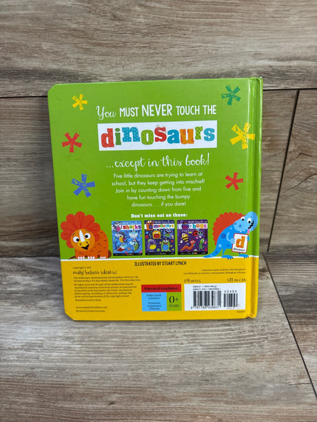 Back of Never Touch the Dinosaurs board book showing green cover with colorful title, dinosaurs and barcode on wood floor