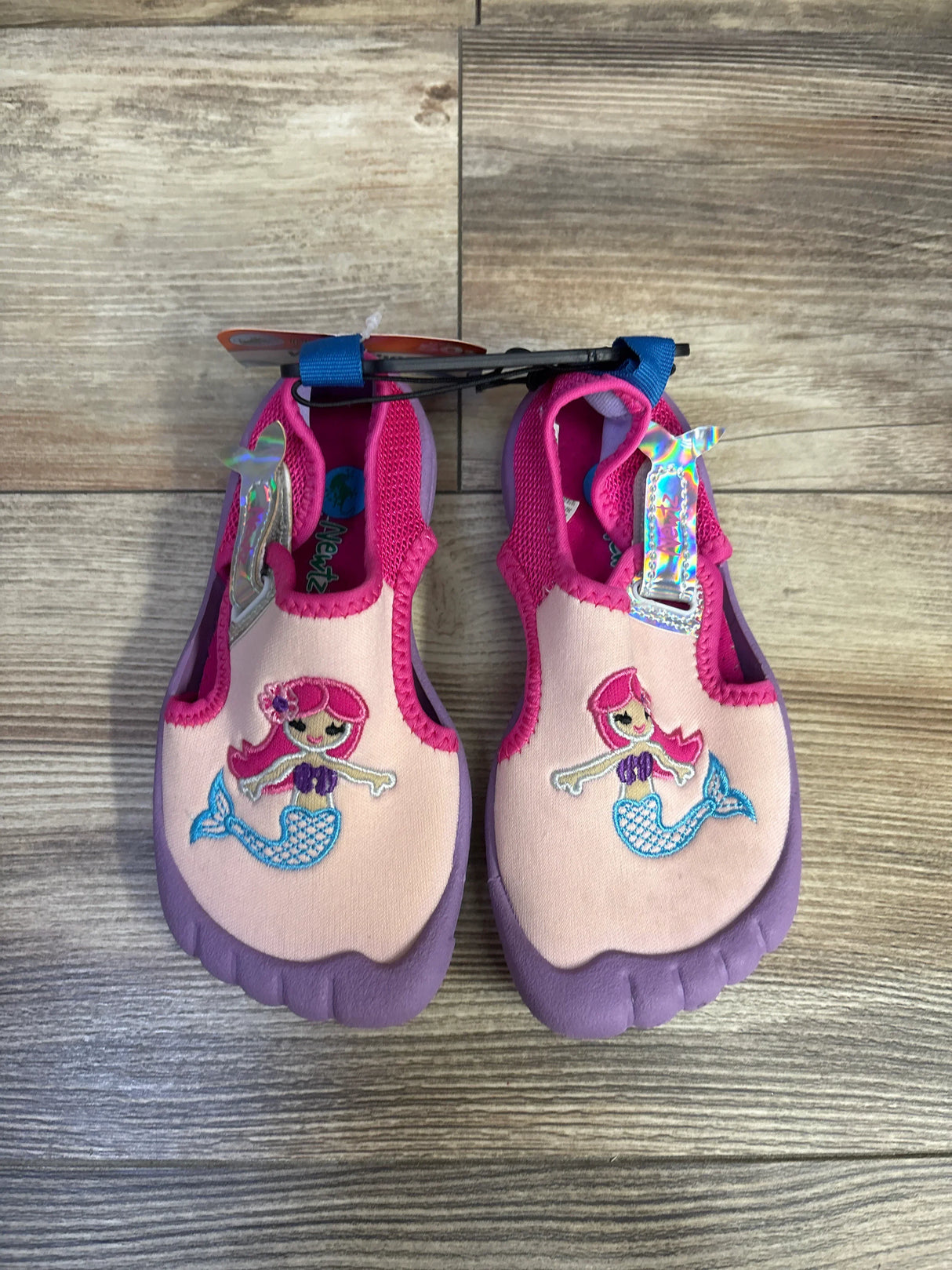 Top-down view of toddler water shoes showcasing embroidered mermaid on pink upper and purple rubber sole with wood floor background