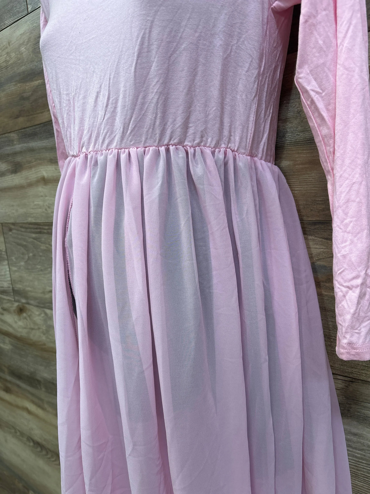 Front close-up of pink maternity maxi dress showing long sleeve, gathered empire waist and sheer skirt on wood background