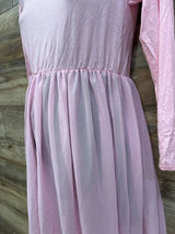 Front close-up of pink maternity maxi dress showing long sleeve, gathered empire waist and sheer skirt on wood background