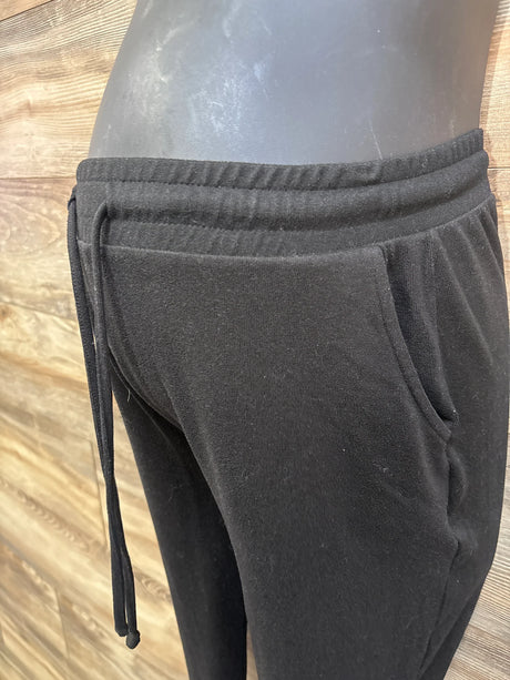 Side view of black maternity drawstring joggers showing elastic waistband and side pocket on mannequin against wood backdrop