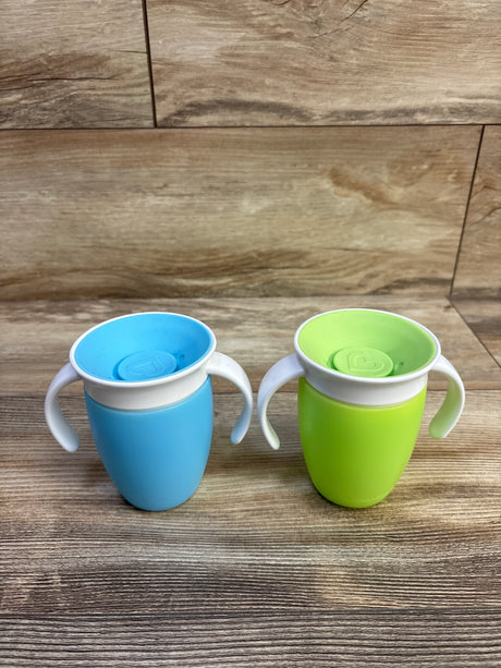 Front view of two Munchkin Miracle 360 trainer cups (7 oz) showcasing white handles and 360-degree spill-proof lids on wood tabletop