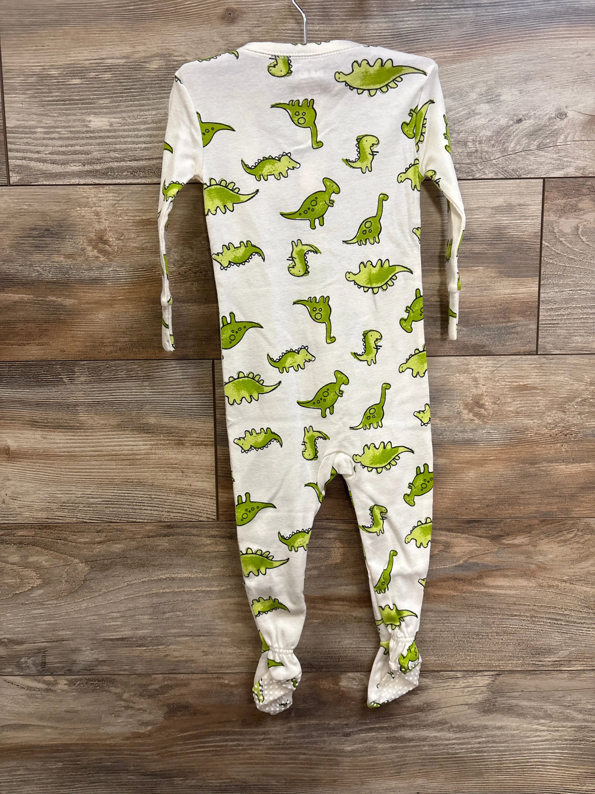 Back view of white Old Navy footed sleeper with green dinosaur print, size 12-18 months, hanging on wooden background