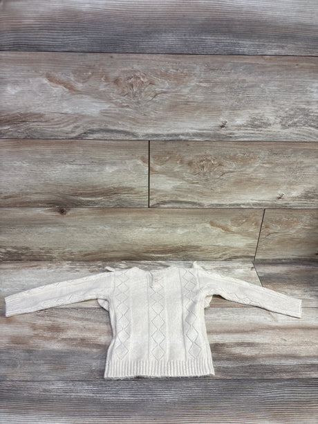 Front view of beige knit ruffle sweater in size 18 to 24 months showcasing diamond knit panels and button placket on wood flooring
