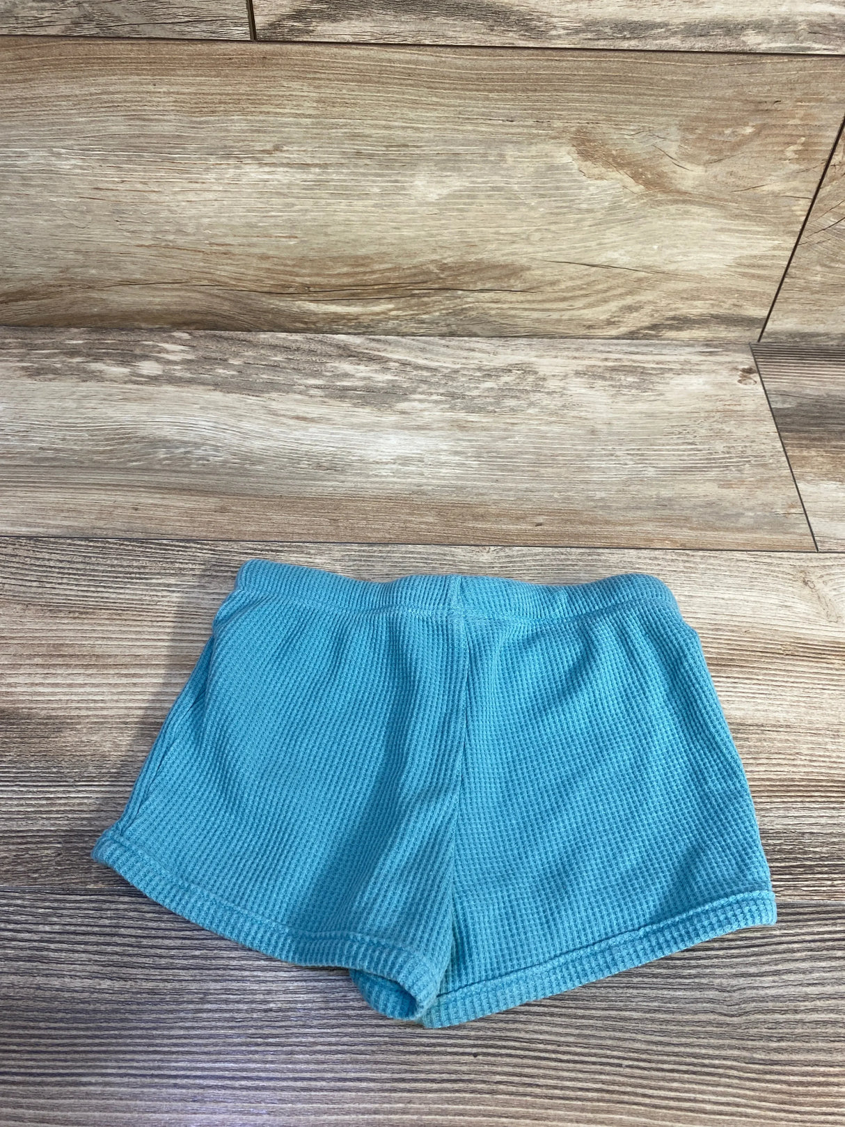 Top-down view of teal Cat and Jack toddler shorts showing elastic waistband and waffle texture on wood background