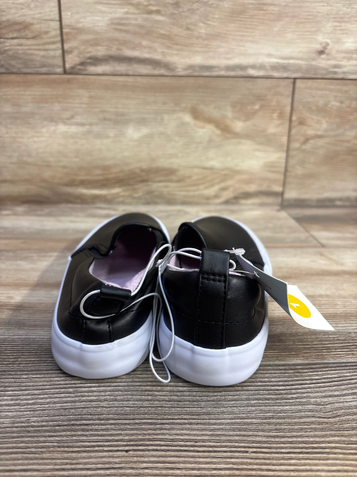 Rear view of Cat & Jack Hailey toddler slip-on sneakers, black with white soles and pink lining on wood floor