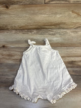 Flat lay of ivory baby tank shortie romper showing knotted shoulder straps and ruffle hem at legs on wood background
