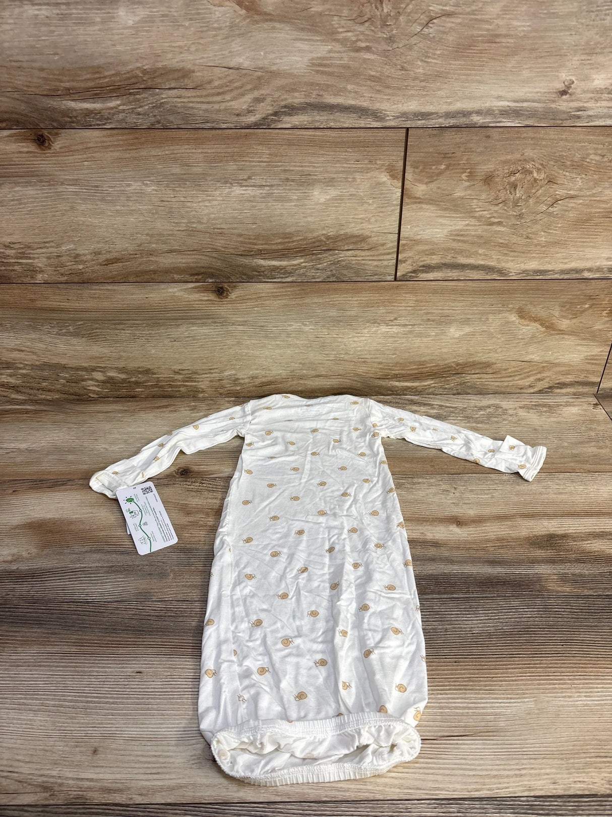 Flat lay of Carter's PurelySoft white infant gown showing tan snail print, long sleeves and elastic gathered bottom on wood surface